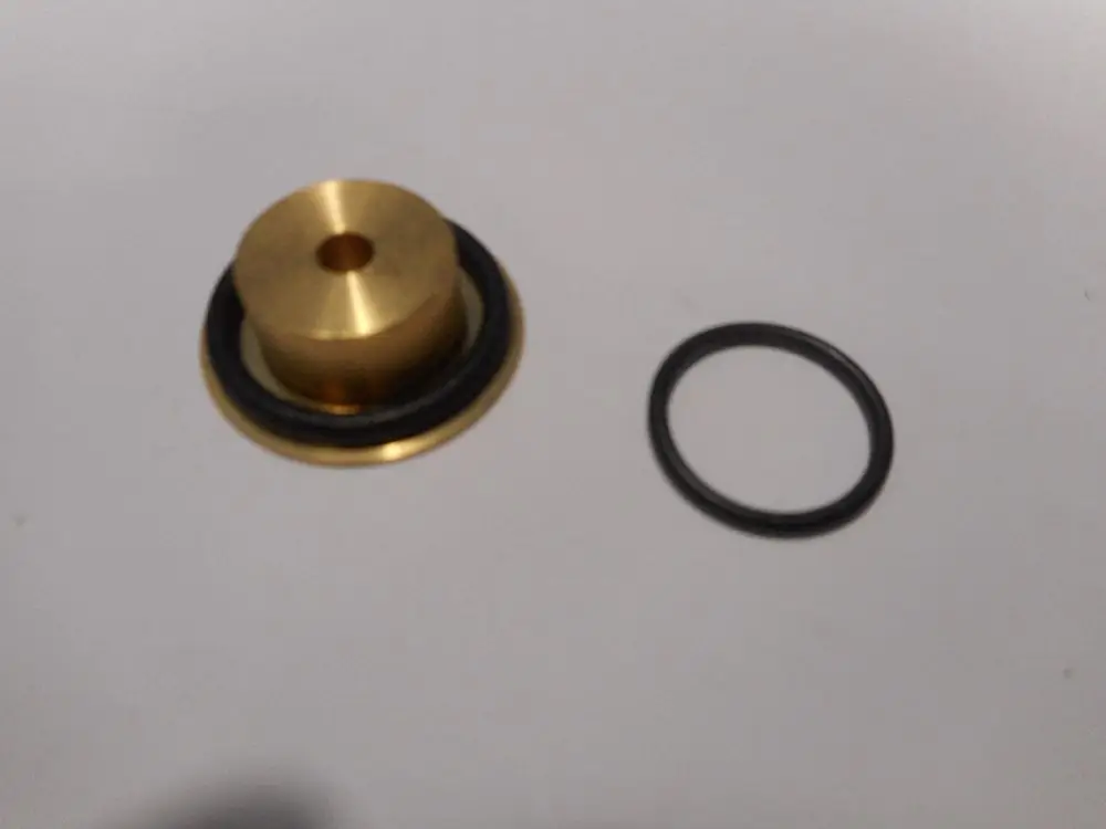 Düse mit metallischem Körper und Gummidichtung, geeignet für Anwendungen von Remeha, liegt neben einem schwarzen O-Ring auf einem weißen Hintergrund.